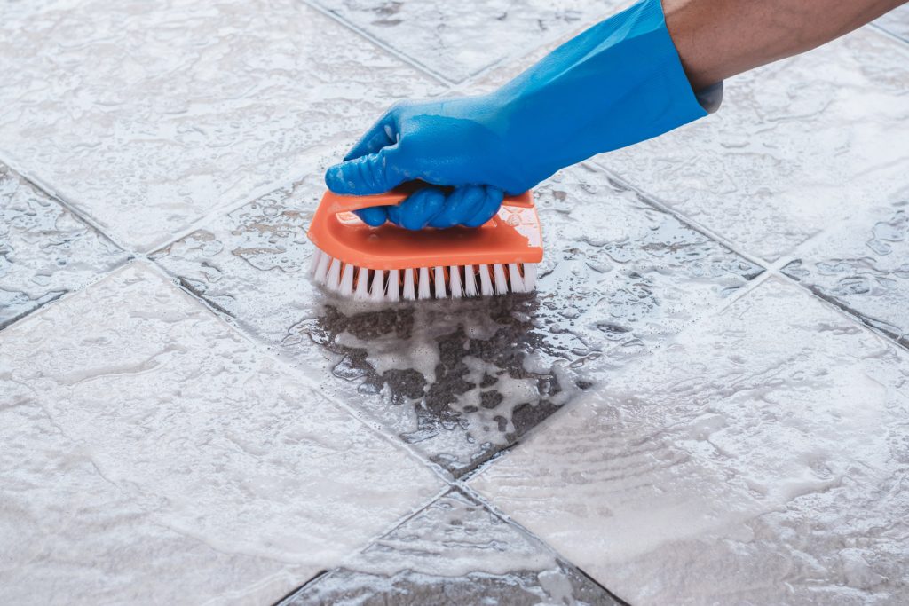 Gloved arm holding brush to clean tiles